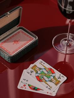 a glass of wine and playing cards on a table with a pair of red glasses