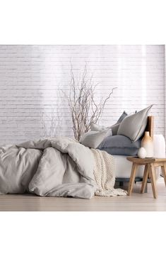 an unmade bed sitting in front of a white brick wall with pillows and blankets on it