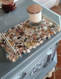 there is a candle and some seashells on the side of a table with a glass container