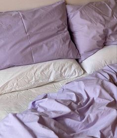 an unmade bed with purple sheets and pillows