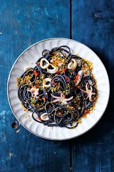 a white plate topped with black pasta and toppings on top of a blue wooden table