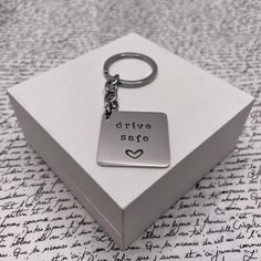 a silver square keychain with the words drive safe on it sitting in a box