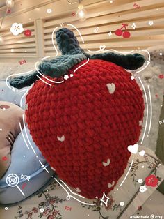 a red knitted strawberry pillow on top of a bed with hearts and flowers around it