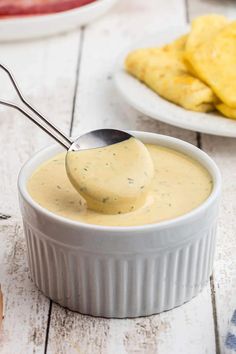 a spoon full of cheese sauce on top of a white bowl with tortilla chips in the background