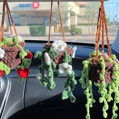 three crocheted plants hanging from hooks in the dashboard of a car with other decorations