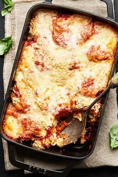 a casserole dish with meat and cheese in it on a cloth next to a spoon