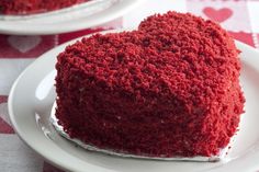 a heart shaped red velvet cake sitting on top of a white plate next to another piece of cake