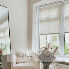 a white chair sitting in front of a window next to a vase filled with flowers