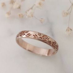 a rose gold wedding ring on top of a white table with flowers in the background