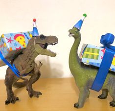 two toy dinosaurs wearing birthday hats and carrying gifts