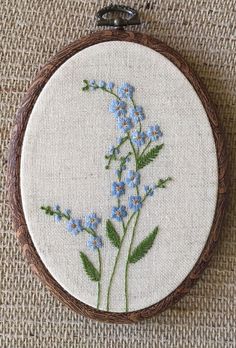 blue flowers are embroidered onto the back of a white fabric hoop hanging from a wooden frame