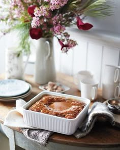 a table topped with a white dish filled with food next to a vase full of flowers