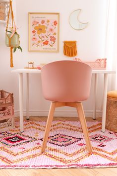 a pink chair sitting on top of a rug in front of a white desk and wall