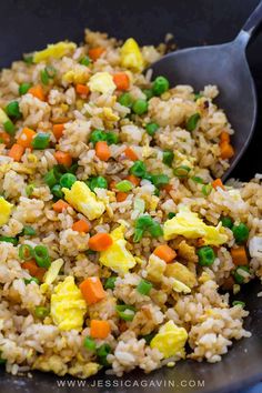 rice and vegetables are mixed in a skillet with a serving spoon on the side