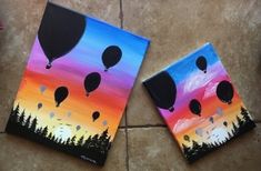 two paintings with hot air balloons in the sky and trees painted on them, sitting on a tile floor