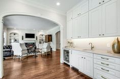 a large kitchen with white cabinets and wood flooring, along with an archway leading to the living room