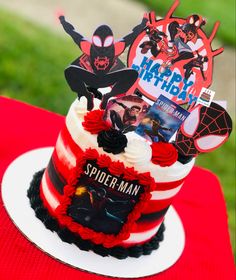 a spiderman themed birthday cake on a red and white tablecloth with the words happy birthday