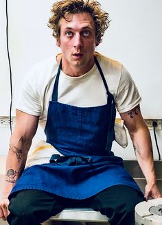 a man sitting on top of a counter wearing an apron