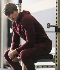 a young man sitting on top of a bench in front of a gym equipment rack