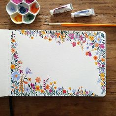 an artist's notebook with watercolors, paint and brushes next to it