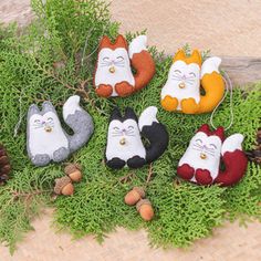 the cat ornaments are hanging on the tree branch in front of pine cones and needles