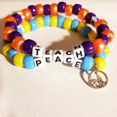 two bracelets with charms that say teach, peace and peace is spelled in white letters