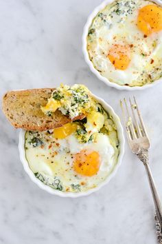 two bowls filled with eggs and bread on top of a white tablecloth next to a fork