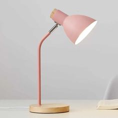 a pink desk lamp sitting on top of a white table next to an open book