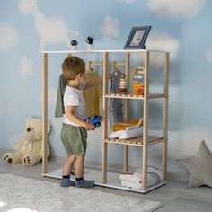 a little boy standing in front of a shelf with clothes and toys on top of it