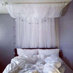 an unmade bed with white sheets and lights hanging from the headboard above it