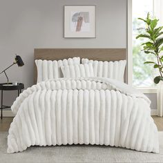 a bed covered in white blankets next to a window with a potted plant on the side