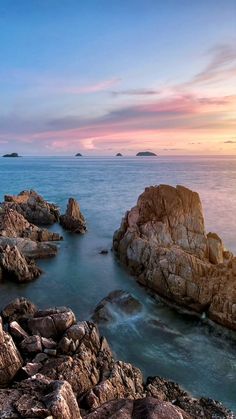 the sun is setting over some rocks in the ocean