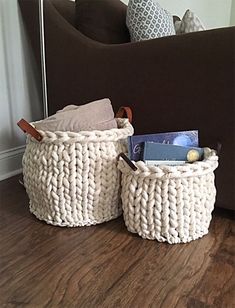 two white baskets sitting on top of a wooden floor next to a brown couch and pillows