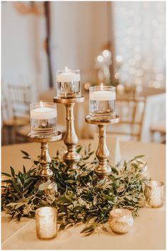 candles are sitting on top of a table with greenery in front of the candle holders