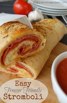 a sandwich cut in half sitting on top of a cutting board next to a bowl of tomato sauce