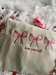 three pink bows on a white cloth with the words love yourself written in red ink