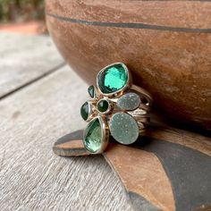 This sterling silver ring is perfect for the person who loves green semi-precious gemstones, and especially in different forms. The ring was made by one of the most beloved Albuquerque designers, Lilly Barrack, and it consists of a thick wire sterling silver band atop which sit seven smooth bezels, each with a green gemstone in a color palette that tends toward the forest-slash-emerald tones. There are two druzies, three opaque jade tone stones, and the two largest are faceted and display more clairty. With the thick sterling silver wraparound band and those various gemstones, the piece conjures images of forests and moss. The end result is a modernist and uncommon statement-cocktail ring. This ring was made when Barrack was a practicing artist, during the late 1990s to early 2000s. From h Green Multi-stone Emerald Rings, Fine Jewelry Green Stackable Jewelry, Green Gemstone Stackable Rings For May Birthstone, Fine Green Stackable Jewelry, Green Emerald Fusion Ring, Green Emerald Fusion Style Ring, Green Stackable Fine Jewelry, Green Multi-stone Gemstones Fine Jewelry, Green Multi-stone Fine Jewelry Gemstones