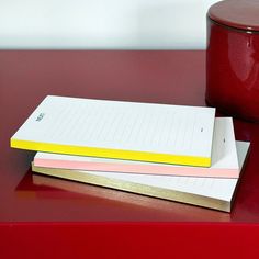 two notebooks are sitting on top of a red table next to a canister