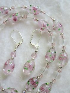 "This lampworked pink jewelry set is made with 14mm round frosted ovals with pink inlaid flowers. The 20\" necklace has a 3\" silver plated extender. Each oval is set off with silver plated heishe beads. Frosted 8mm rounds and pink bi-cone crystals are used between each lampwork bead. These beads are beautifully delicate and make a fine gift. The matching earrings dangle 1\" from the loops of the silver plated lever back wires. This set will be slipped into an organza bag and shipped in a bubble Elegant Pink Czech Glass Necklaces, Pink Flower-shaped Jewelry With Dangling Beads, Pink Multi-strand Faceted Bead Necklace, Pink Jewelry Set, Elegant Pink Multi-stone Necklace, Pink Multi-strand Faceted Beads Jewelry, Blue Jewelry Set, Lampwork Jewelry, Pink Jewelry