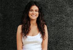 a woman standing in front of a wall with her hands on her hips and looking at the camera