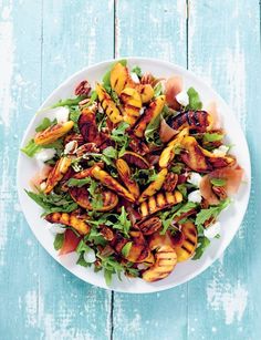 grilled peaches and greens in a white bowl on a blue wooden table top