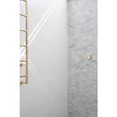 a bathroom with a walk in shower next to a white tiled wall and gold fixtures