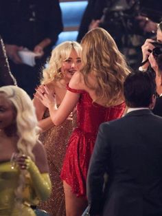 two women in red dresses hugging each other at the oscars, with cameras around them