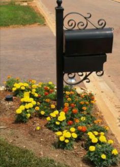 a mailbox sitting in the middle of a flower bed next to a street and sidewalk