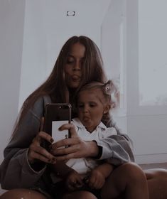 a woman sitting on the floor holding a baby and looking at her cell phone screen