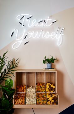 a wooden shelf filled with lots of different types of nuts and plants next to a neon sign that says treat yourself