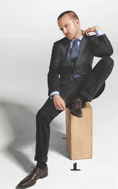 a man in a suit and tie sitting on top of a wooden block with his hands behind his head