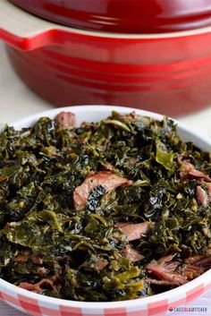 a bowl filled with meat and greens next to a red casserole dish on a table