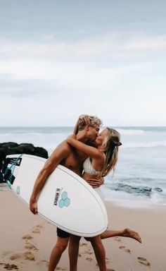 a man and woman kissing on the beach with a surfboard in their hands,