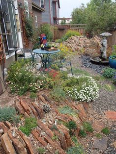 a garden with rocks and flowers on the ground next to a patio chair, table and umbrella